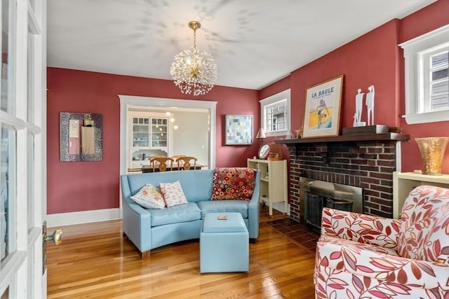 living area featuring a brick fireplace, a notable chandelier, baseboards, and wood finished floors