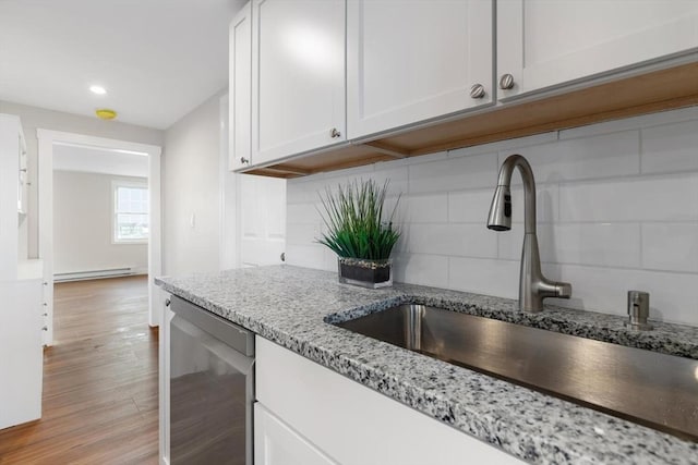 kitchen with tasteful backsplash, sink, white cabinets, baseboard heating, and light stone counters