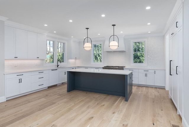 kitchen with a kitchen island, light countertops, custom range hood, white cabinets, and light wood-type flooring