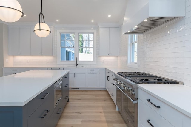 kitchen with custom exhaust hood, a sink, stainless steel stove, light countertops, and light wood-style floors