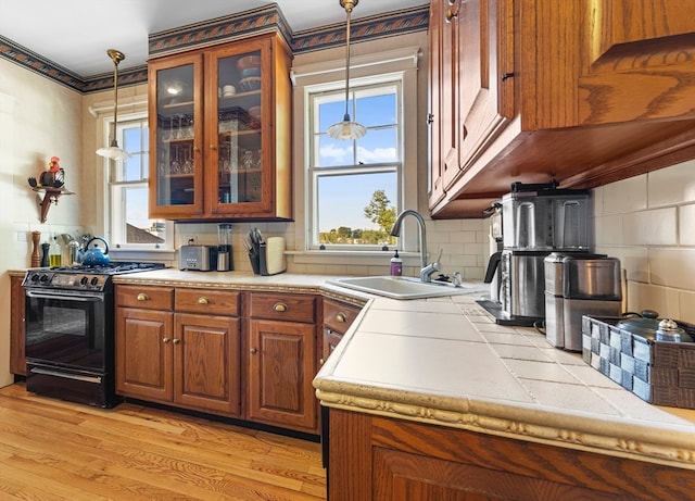 kitchen featuring light hardwood / wood-style floors, tasteful backsplash, black range with gas cooktop, decorative light fixtures, and sink