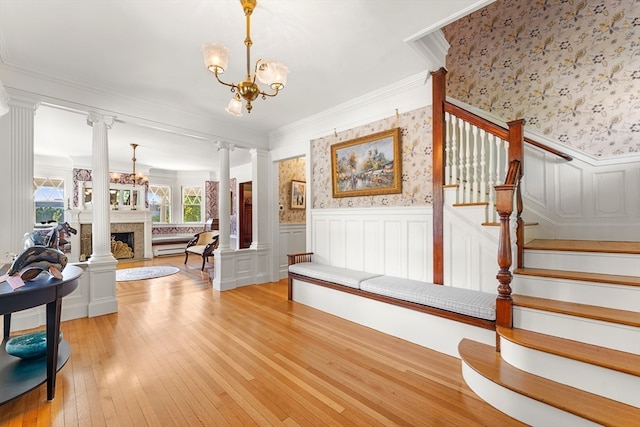 foyer entrance featuring light hardwood / wood-style floors, a notable chandelier, decorative columns, baseboard heating, and crown molding