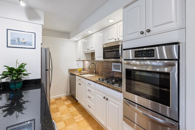 kitchen with a warming drawer, stainless steel appliances, tasteful backsplash, white cabinets, and a sink