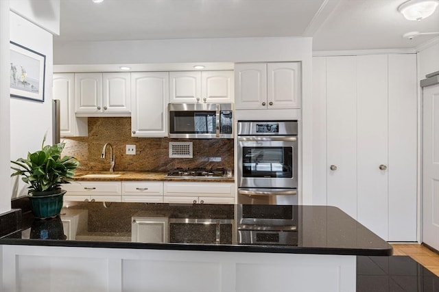 kitchen featuring dark stone countertops, white cabinetry, stainless steel appliances, and a sink