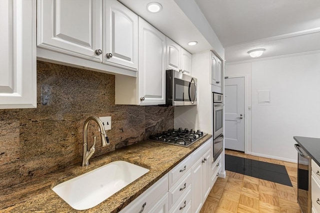 kitchen with a sink, white cabinets, appliances with stainless steel finishes, backsplash, and dark stone countertops