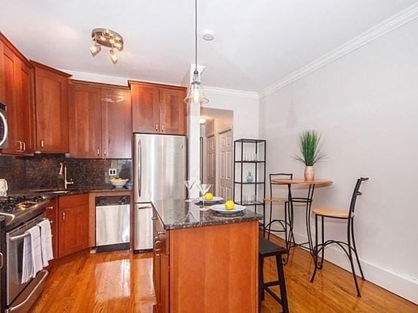 455 Massachusetts Ave Unit 2, Boston, MA 02118 - kitchen with stainless steel appliances, wood finished floors, decorative backsplash, ornamental molding, and a breakfast bar