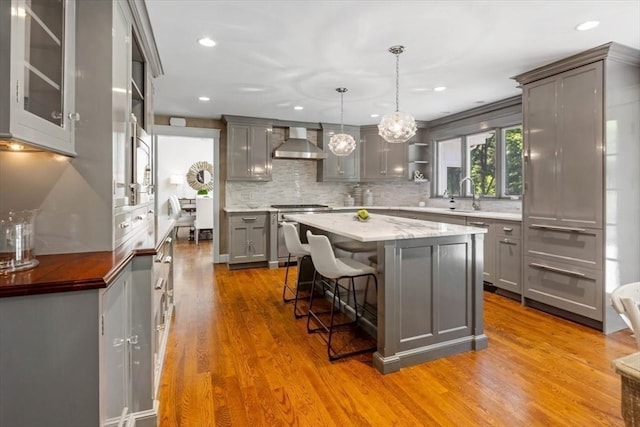 kitchen with gray cabinetry, wall chimney range hood, light wood-type flooring, pendant lighting, and a center island