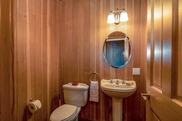 bathroom featuring toilet, wood walls, and sink