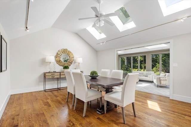 dining area with light hardwood / wood-style floors, ceiling fan, rail lighting, and lofted ceiling with skylight