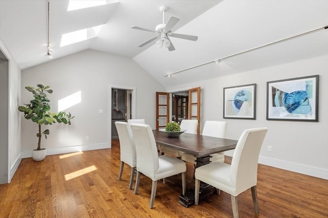 dining room featuring lofted ceiling with skylight, rail lighting, ceiling fan, and light hardwood / wood-style flooring