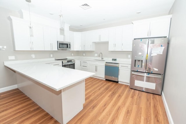 kitchen with a peninsula, a sink, light wood-style floors, light countertops, and appliances with stainless steel finishes