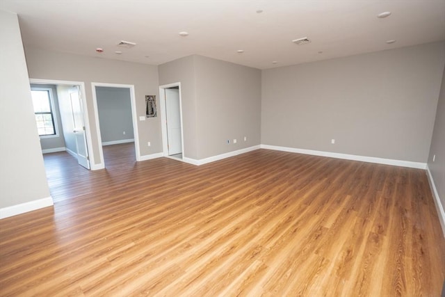 spare room with light wood-type flooring, visible vents, and baseboards