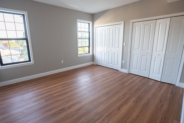 unfurnished bedroom featuring baseboards, dark wood-type flooring, and multiple closets