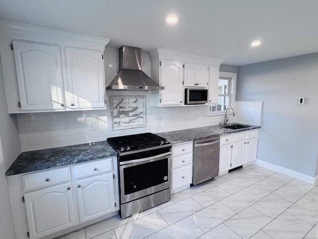 kitchen with wall chimney range hood, white cabinetry, appliances with stainless steel finishes, and a sink