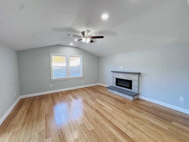 unfurnished living room with baseboards, a ceiling fan, lofted ceiling, a stone fireplace, and light wood-style floors