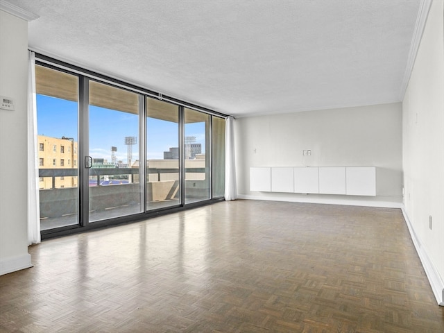 unfurnished room featuring a textured ceiling, floor to ceiling windows, ornamental molding, and parquet floors