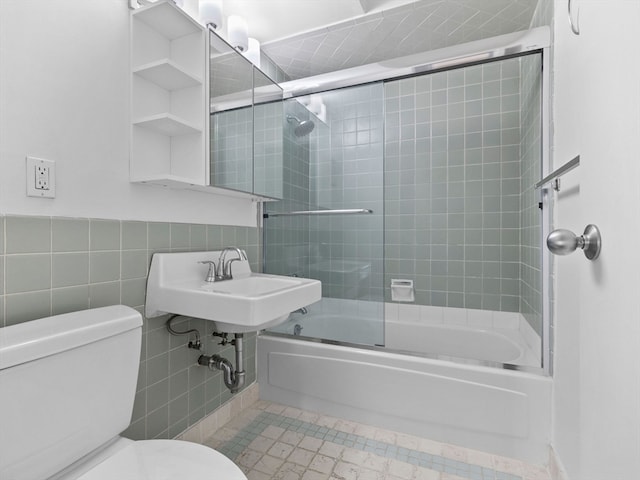 full bathroom featuring shower / bath combination with glass door, sink, tile walls, and toilet