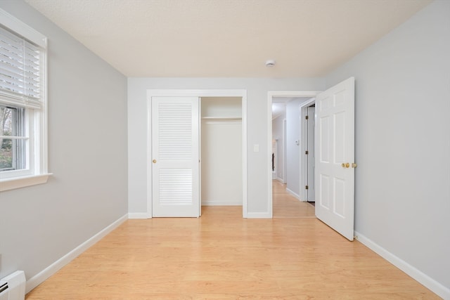 unfurnished bedroom featuring light wood-type flooring, a closet, and baseboard heating