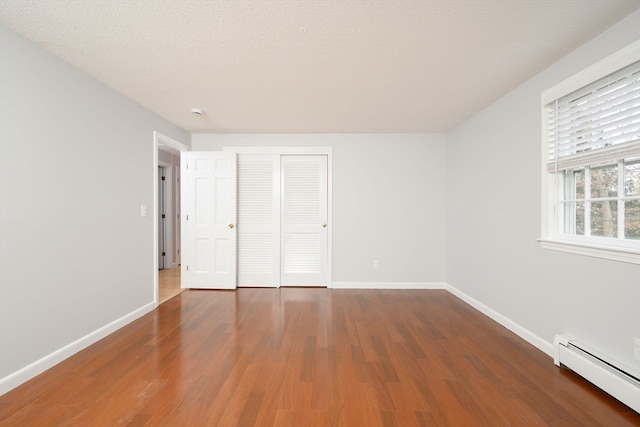 unfurnished bedroom featuring a closet, dark wood-type flooring, a textured ceiling, and a baseboard heating unit