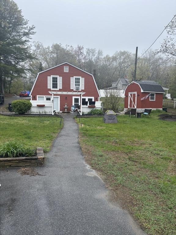 view of front of home with a gambrel roof, a front yard, an outdoor structure, and a shed