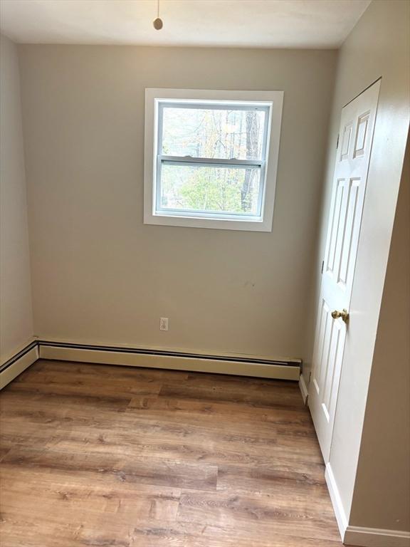 unfurnished room featuring a baseboard heating unit, light wood-style floors, and baseboards