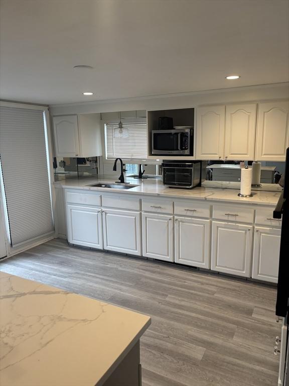 kitchen with a sink, stainless steel microwave, light wood finished floors, white cabinets, and recessed lighting