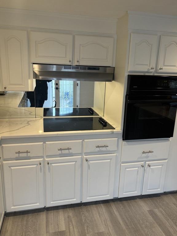 kitchen featuring black appliances, under cabinet range hood, white cabinets, wood finished floors, and ornamental molding