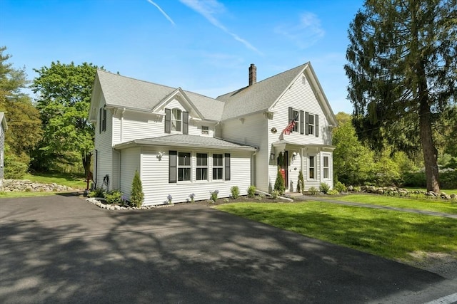 view of front of home with a shingled roof, a chimney, and a front yard