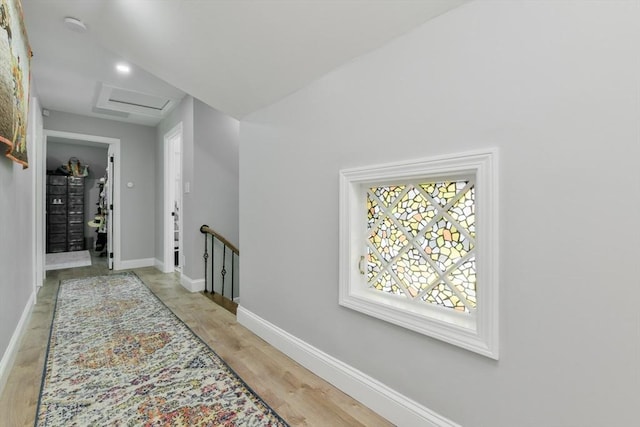 hall featuring attic access, light wood-type flooring, an upstairs landing, and baseboards