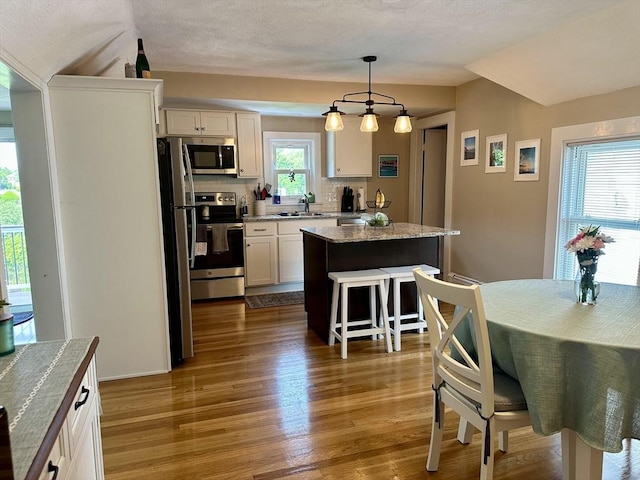3 Centre St, Waltham, MA 02453 - kitchen featuring appliances with stainless steel finishes, a kitchen island, wood finished floors, white cabinets, and a breakfast bar