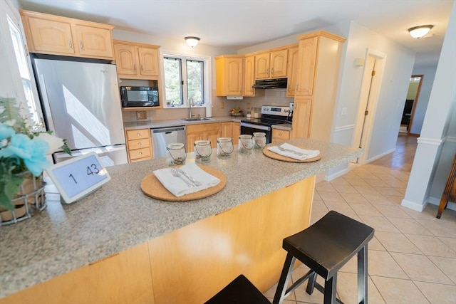 kitchen featuring light brown cabinetry, a sink, under cabinet range hood, appliances with stainless steel finishes, and light tile patterned floors