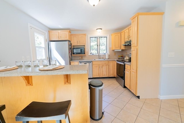 kitchen featuring a sink, light brown cabinets, a kitchen bar, and stainless steel appliances