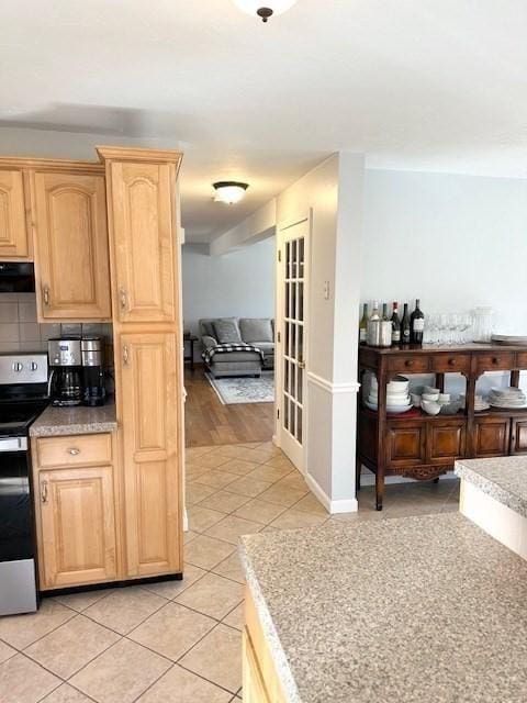 kitchen with light brown cabinets, ventilation hood, light tile patterned floors, decorative backsplash, and stainless steel electric range