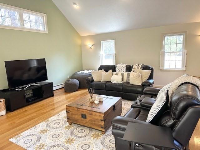 living area featuring a baseboard heating unit, lofted ceiling, wood finished floors, and a wealth of natural light