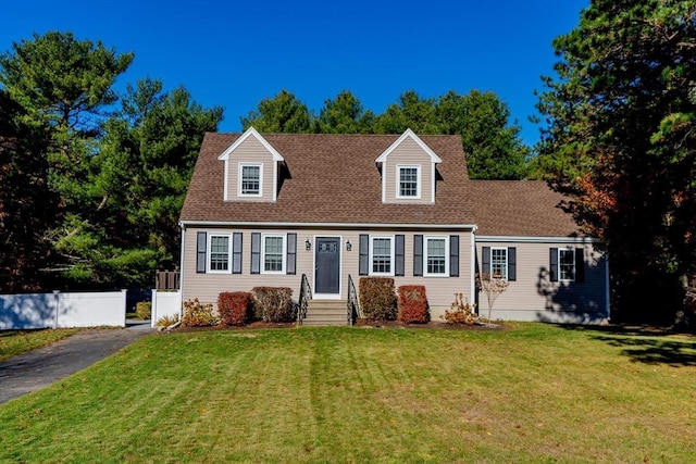 cape cod home with a front yard, fence, and a shingled roof