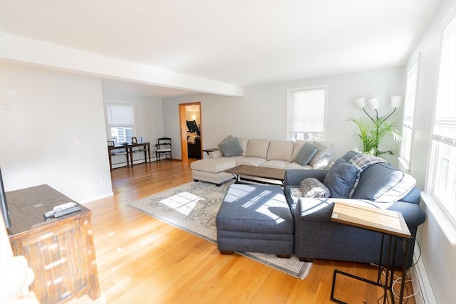 living area featuring beam ceiling, light wood-type flooring, and baseboards