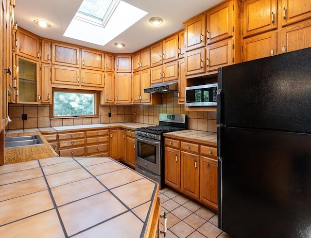 23 Shawmut Ave, Lowell, MA 01851 - kitchen with appliances with stainless steel finishes, tile countertops, under cabinet range hood, a skylight, and backsplash