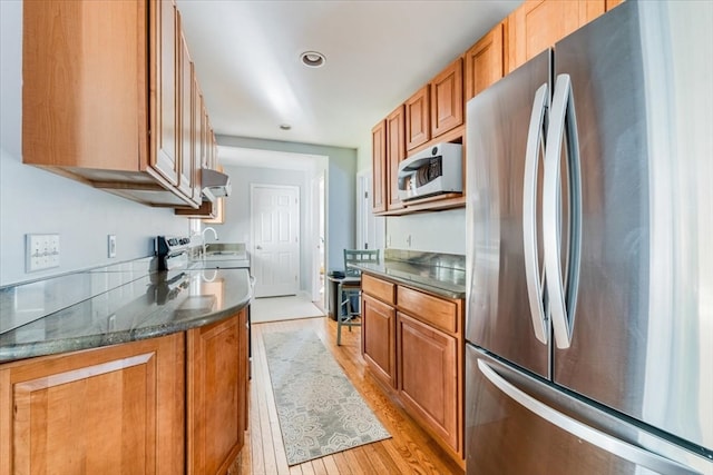 kitchen with dark stone counters, sink, light wood-type flooring, and stainless steel refrigerator