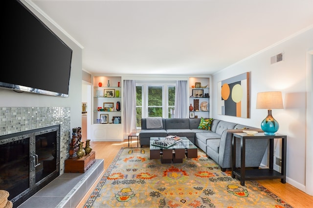 living room featuring ornamental molding, light wood-type flooring, a tile fireplace, and built in shelves