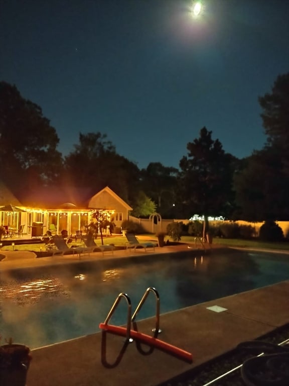 pool at night featuring a patio area