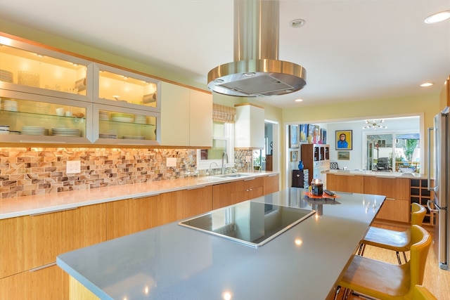 kitchen featuring sink, tasteful backsplash, black electric stovetop, a spacious island, and a breakfast bar area