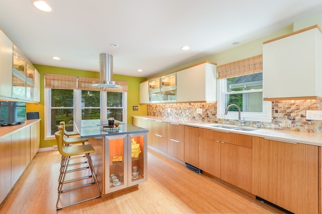 kitchen featuring light hardwood / wood-style floors, white cabinetry, backsplash, a kitchen bar, and sink