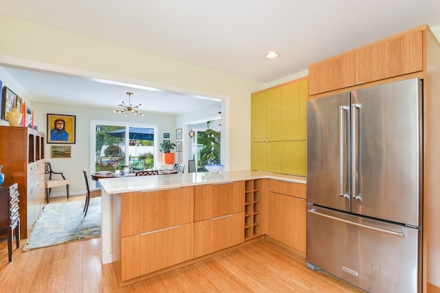 kitchen featuring high quality fridge, a chandelier, kitchen peninsula, and light hardwood / wood-style flooring