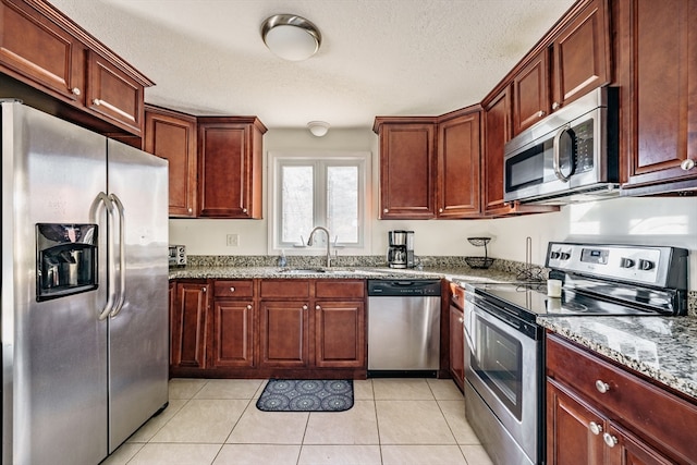 kitchen with light stone counters, stainless steel appliances, a textured ceiling, light tile patterned floors, and sink