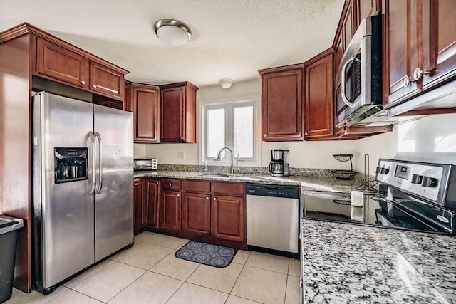 kitchen with light stone counters, light tile patterned flooring, stainless steel appliances, a textured ceiling, and sink