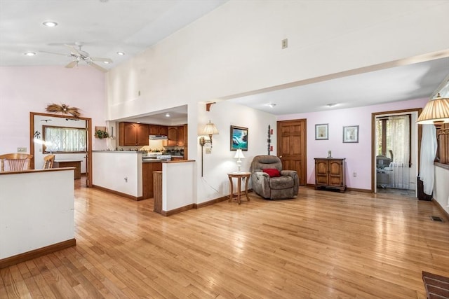 interior space featuring ceiling fan, a towering ceiling, kitchen peninsula, and light wood-type flooring