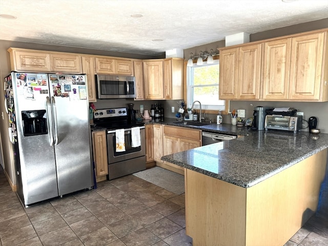 kitchen featuring sink, kitchen peninsula, dark stone counters, a textured ceiling, and appliances with stainless steel finishes