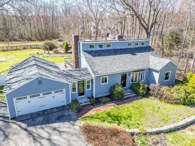 view of front of house featuring a chimney, a shingled roof, driveway, a front lawn, and an attached garage