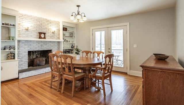 dining space featuring an inviting chandelier, light wood-style flooring, built in features, a brick fireplace, and french doors