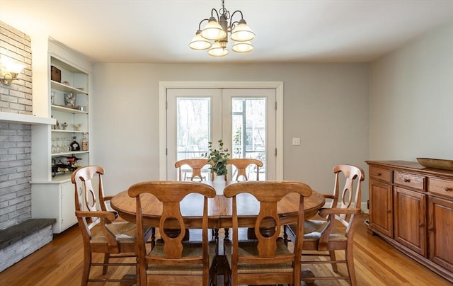 dining room featuring light wood finished floors, an inviting chandelier, built in features, and french doors